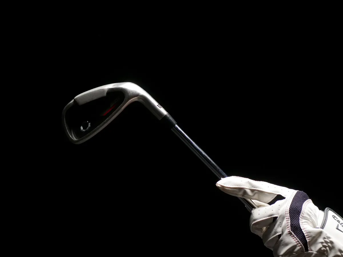 Minimalist image featuring a golf club held by a gloved hand against a black background, highlighting sports equipment.