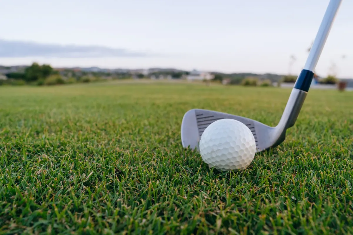 Golf ball with club on lush green grass, perfect for sports themes.