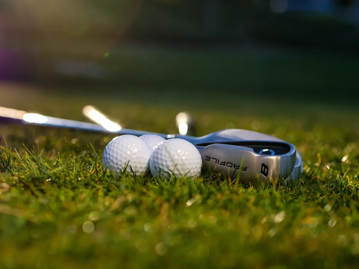 Golf balls and club on a lush green field with warm natural lighting.
