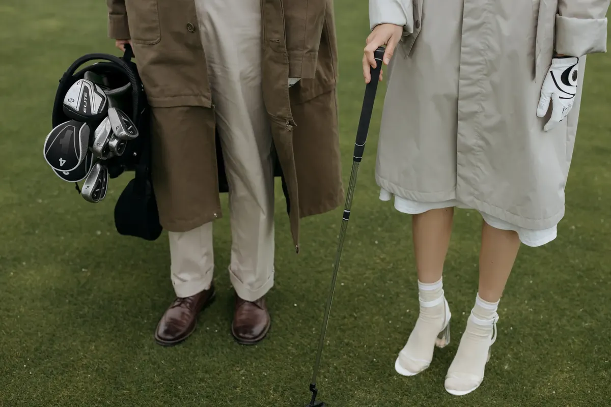 A fashionable couple holding golf clubs and bag on a lush green golf course, showcasing leisure and sports lifestyle.