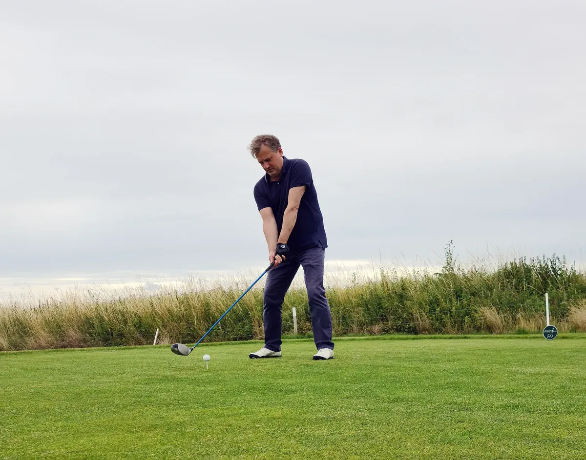 A golfer in action on a lush green golf field in Sweden, wearing a polo shirt and preparing to swing.